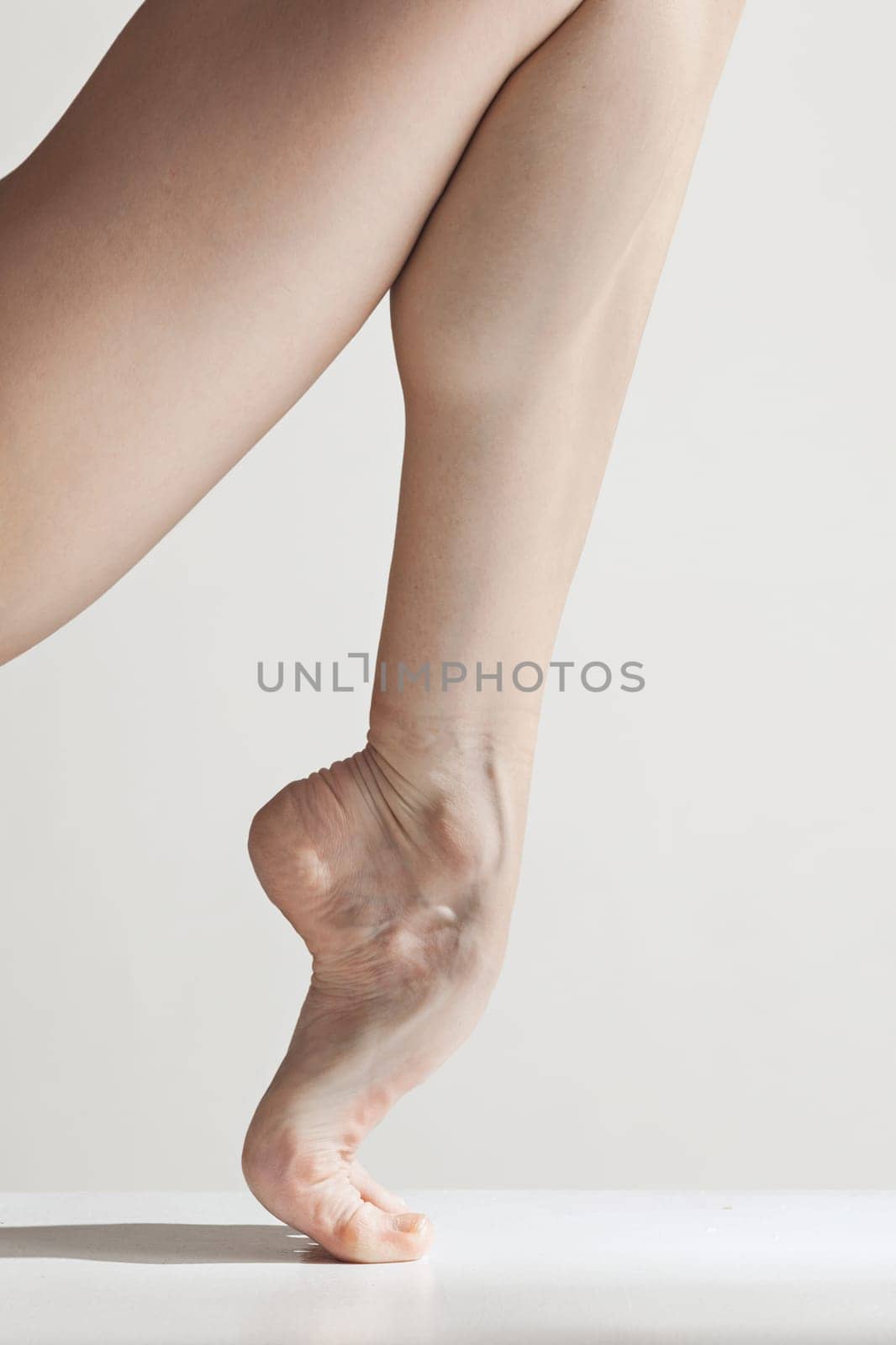 Close-up classic ballerina's legs on the white floor. Young female classical ballet dancer. Ballerina project. Modern choreography, contemporary. Fit caucasian moman. bare feet