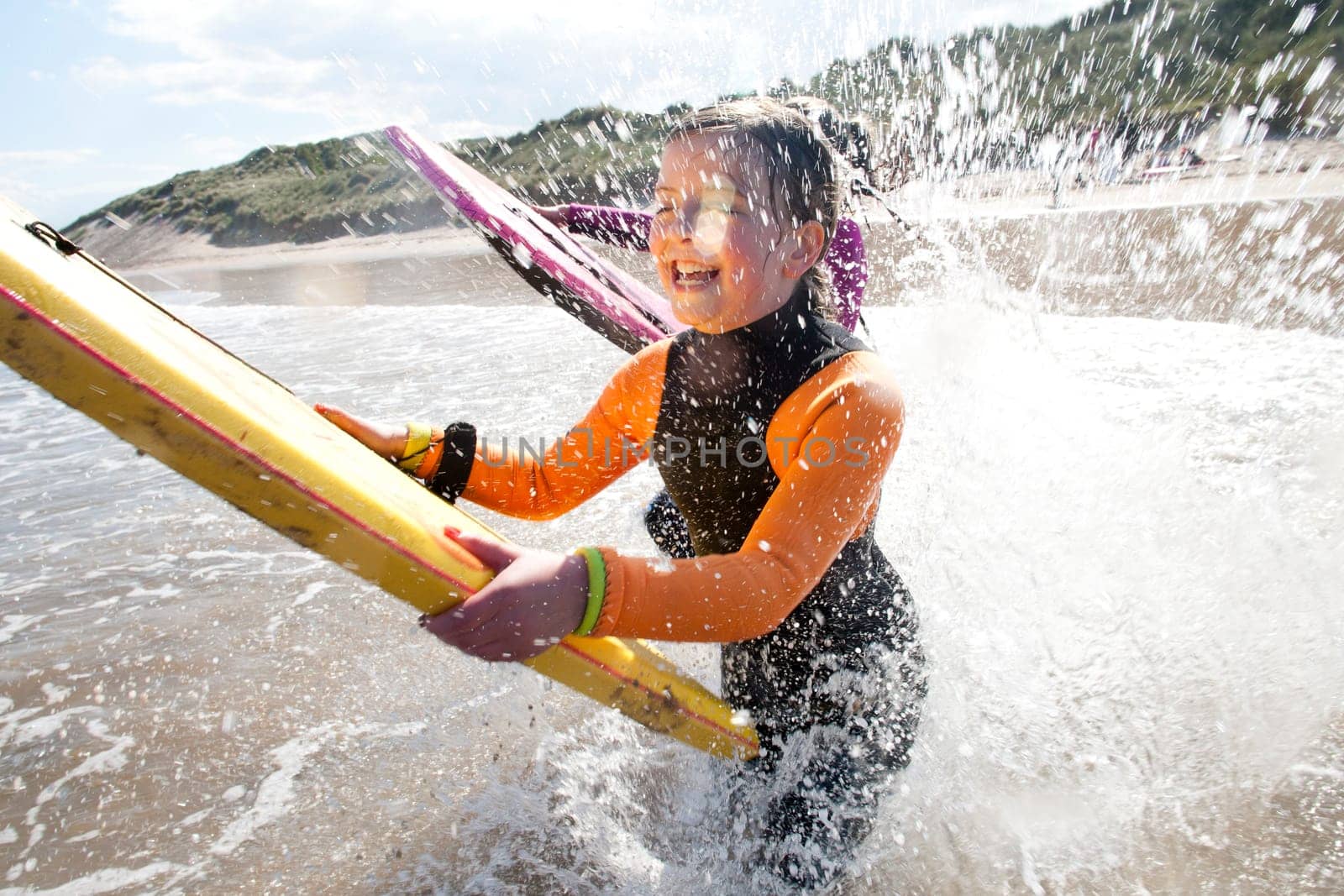 Little girls are splashing in the sea with bodyboards.