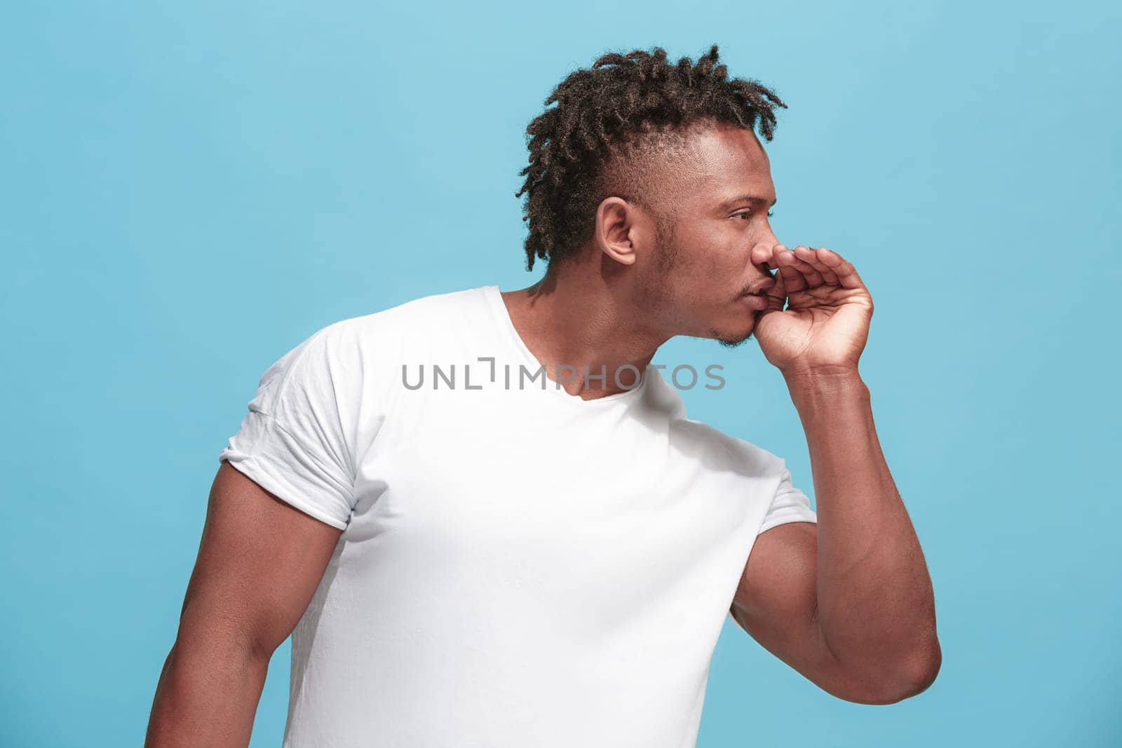Secret, gossip concept. Young man whispering a secret behind his hand. Businessman isolated on trendy blue studio background. Young emotional man. Human emotions, facial expression concept. afro-american. profile