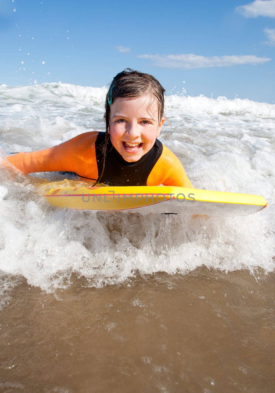 Little girl is smiling for the camera as she bodyboards in the sea.