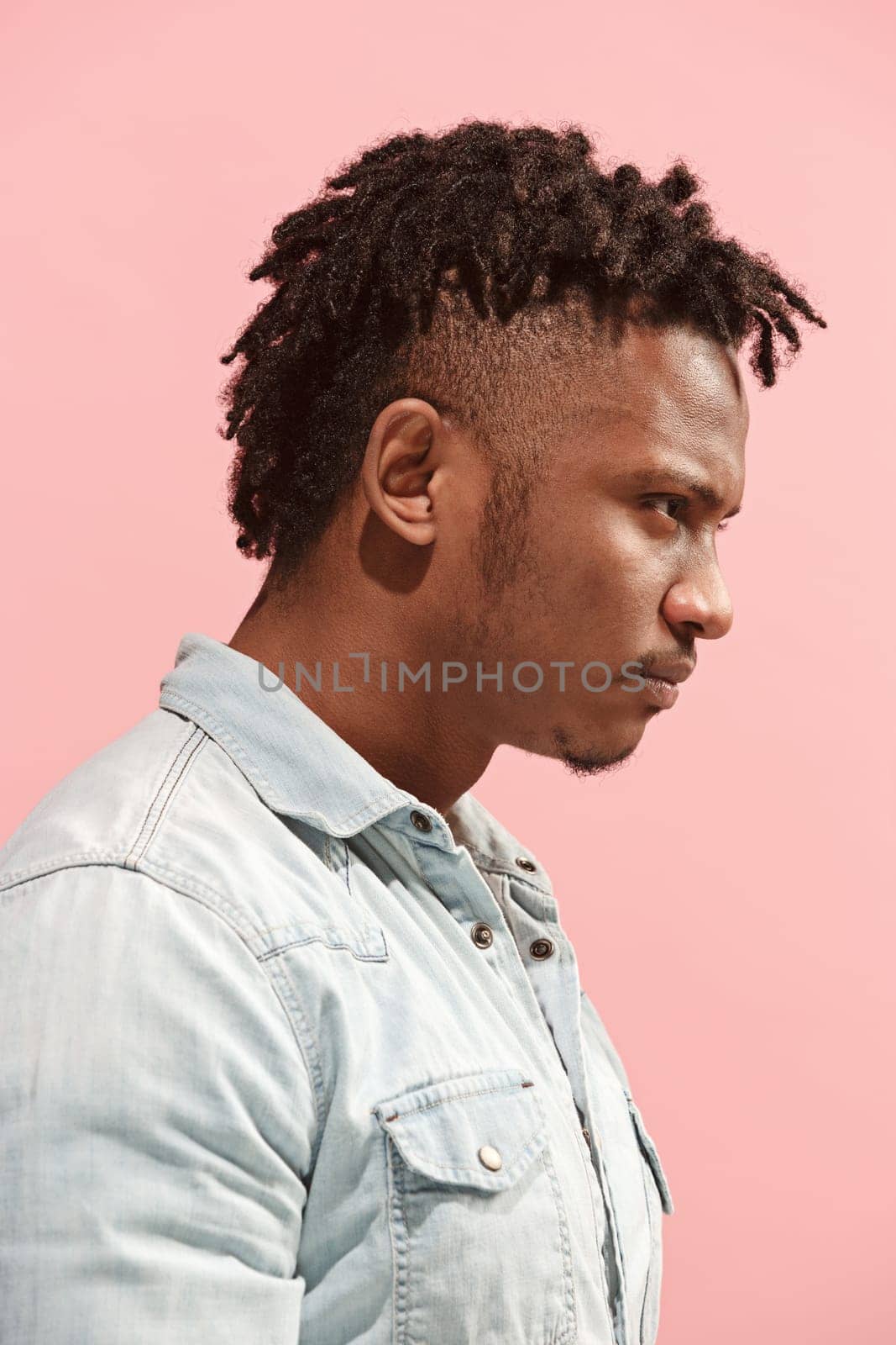 Angry, hate, rage. Emotional angry afro man on pink studio background. Emotional, young face. Profile male half-length portrait. Human emotions, facial expression concept. Trendy colors