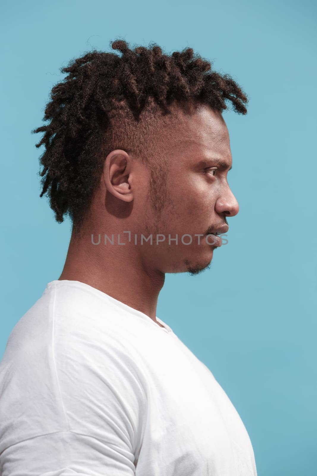 Surprised business Afro-American man standing and looking isolated on blue studio background. African American male profile portrait. Young emotional man. The human emotions, facial expression concept.