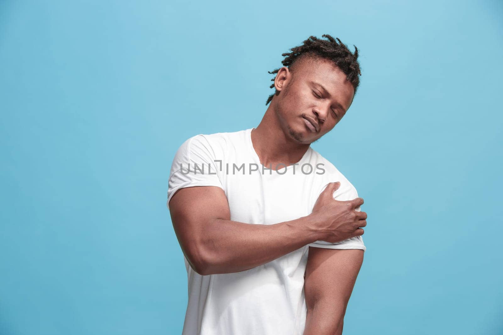 Pain concept. Beautiful afro male portrait isolated on blue backgroud. Young emotional surprised man looking at camera.Human emotions, facial expression concept. man overwhelmed with pain in shoulder