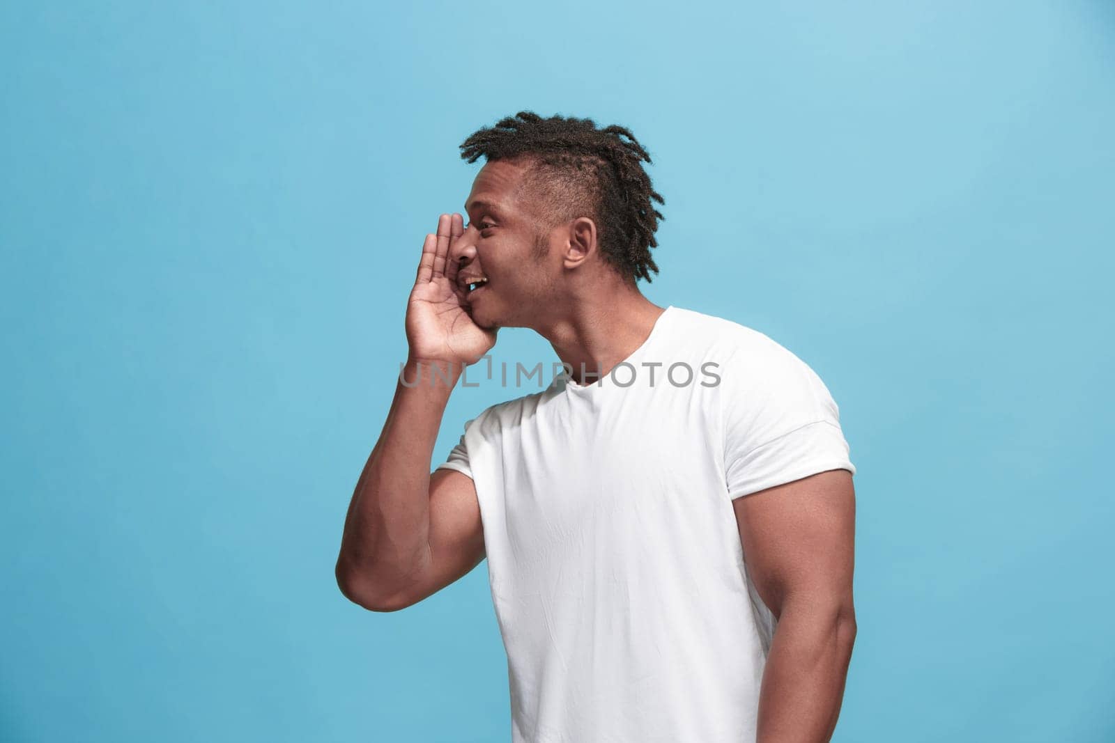 Secret, gossip concept. Young man whispering a secret behind his hand. Businessman isolated on trendy blue studio background. Young emotional man. Human emotions, facial expression concept. afro-american. profile