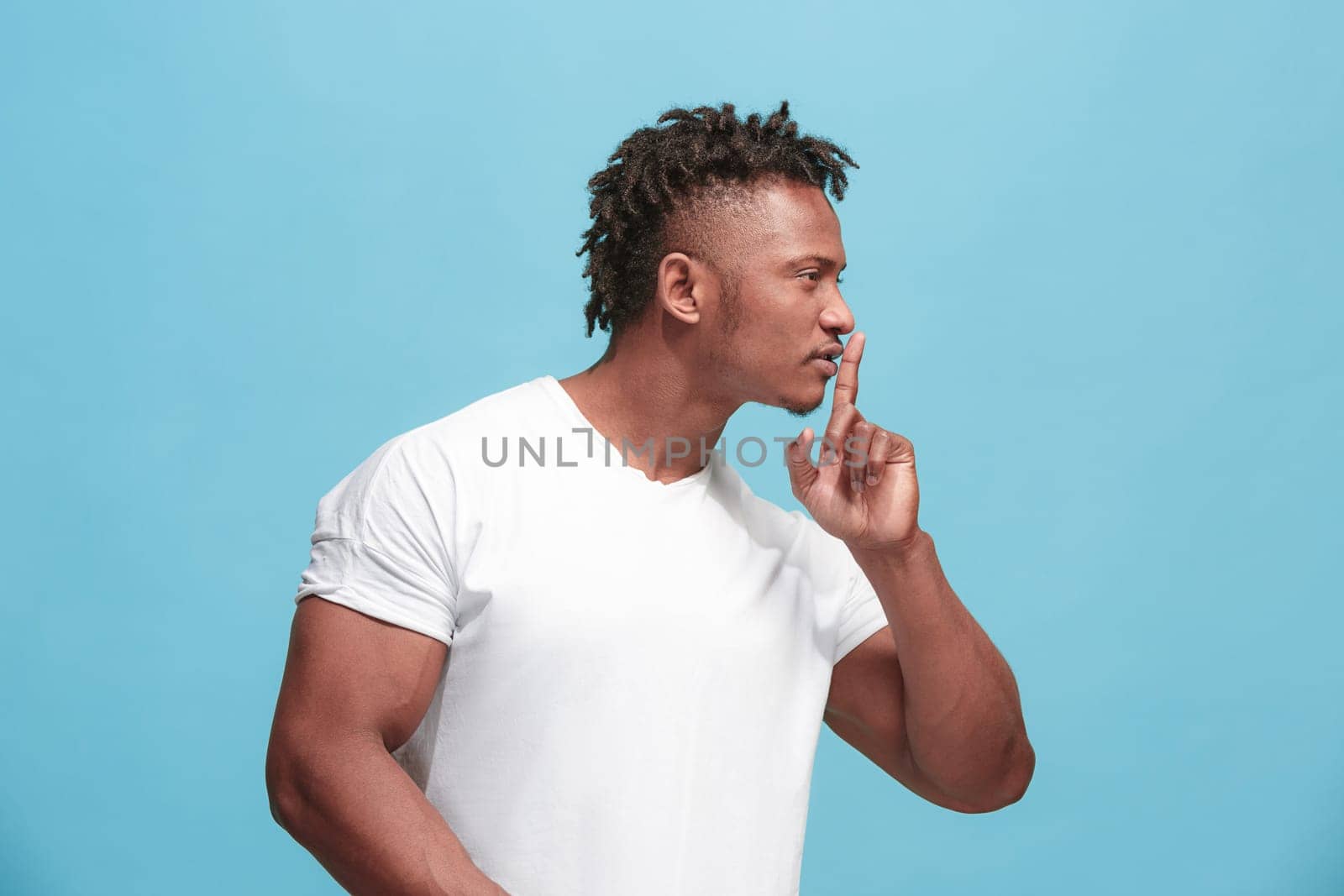 Secret, gossip concept. Young man whispering a secret behind his hand. Businessman isolated on trendy blue studio background. Young emotional man. Human emotions, facial expression concept. afro-american. profile