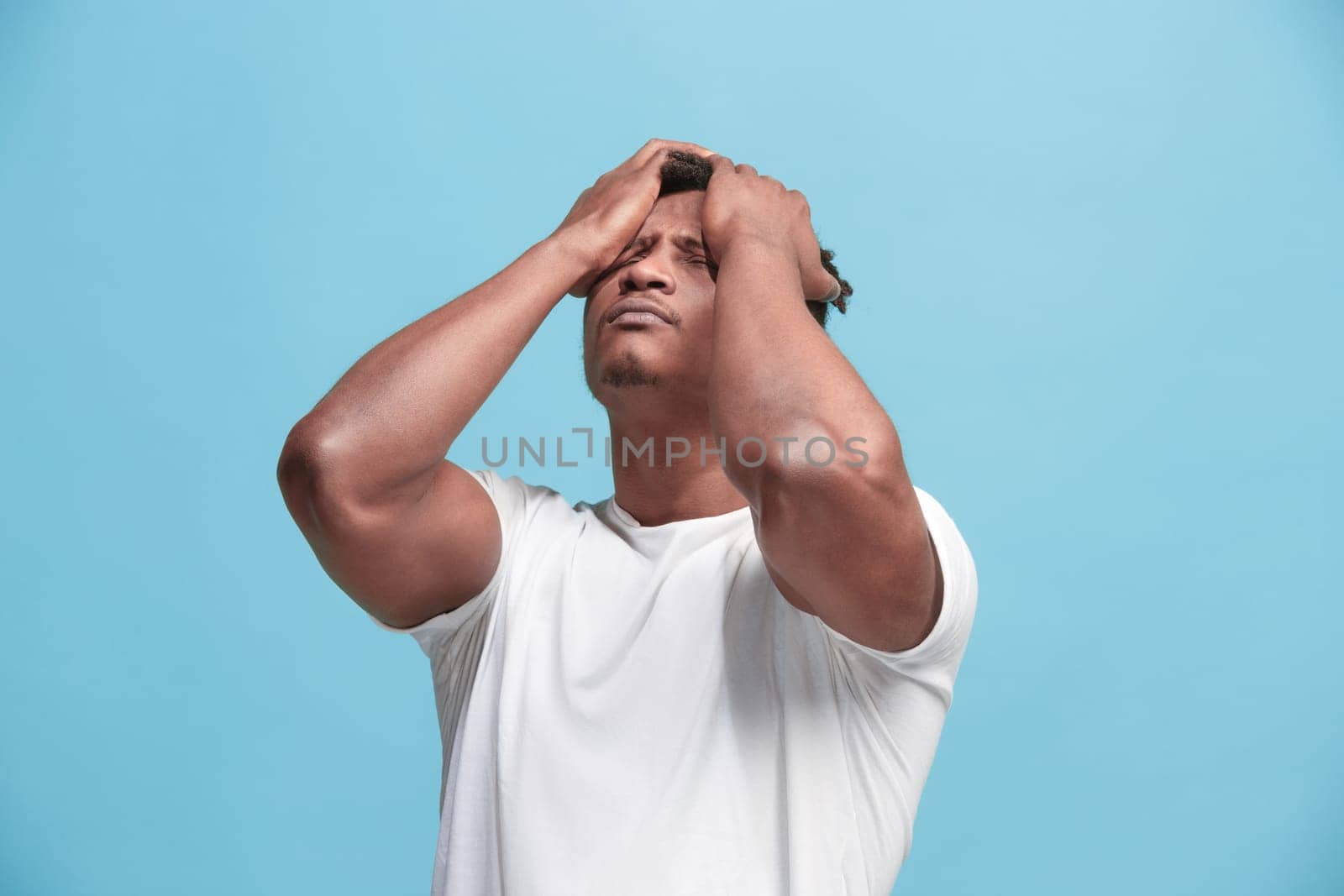 Afro Man having headache. Isolated on blue background. Business man standing with pain isolated on trendy pink studio background. Male half-length portrait. Human emotions, facial expression concept. Front