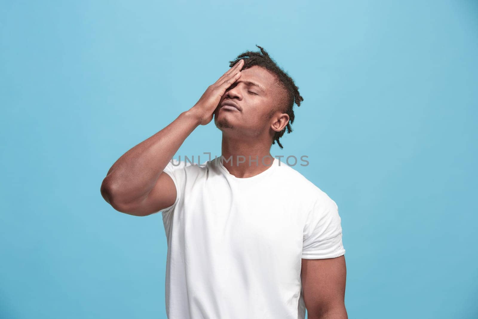 Afro Man having headache. Isolated on blue background. Business man standing with pain isolated on trendy pink studio background. Male half-length portrait. Human emotions, facial expression concept. Front