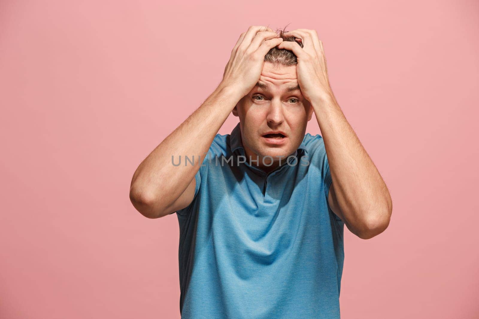 Horrible, stress, shock. Male half-length portrait isolated at pink studio. Young emotional surprised man clasping head in hands. Human emotions, facial expression concept. Trendy colors. Front view
