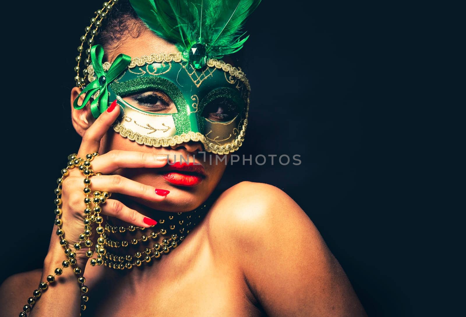 Upscale Indian woman wearing gold jewellery and red lipstick on black background. Green party mask.