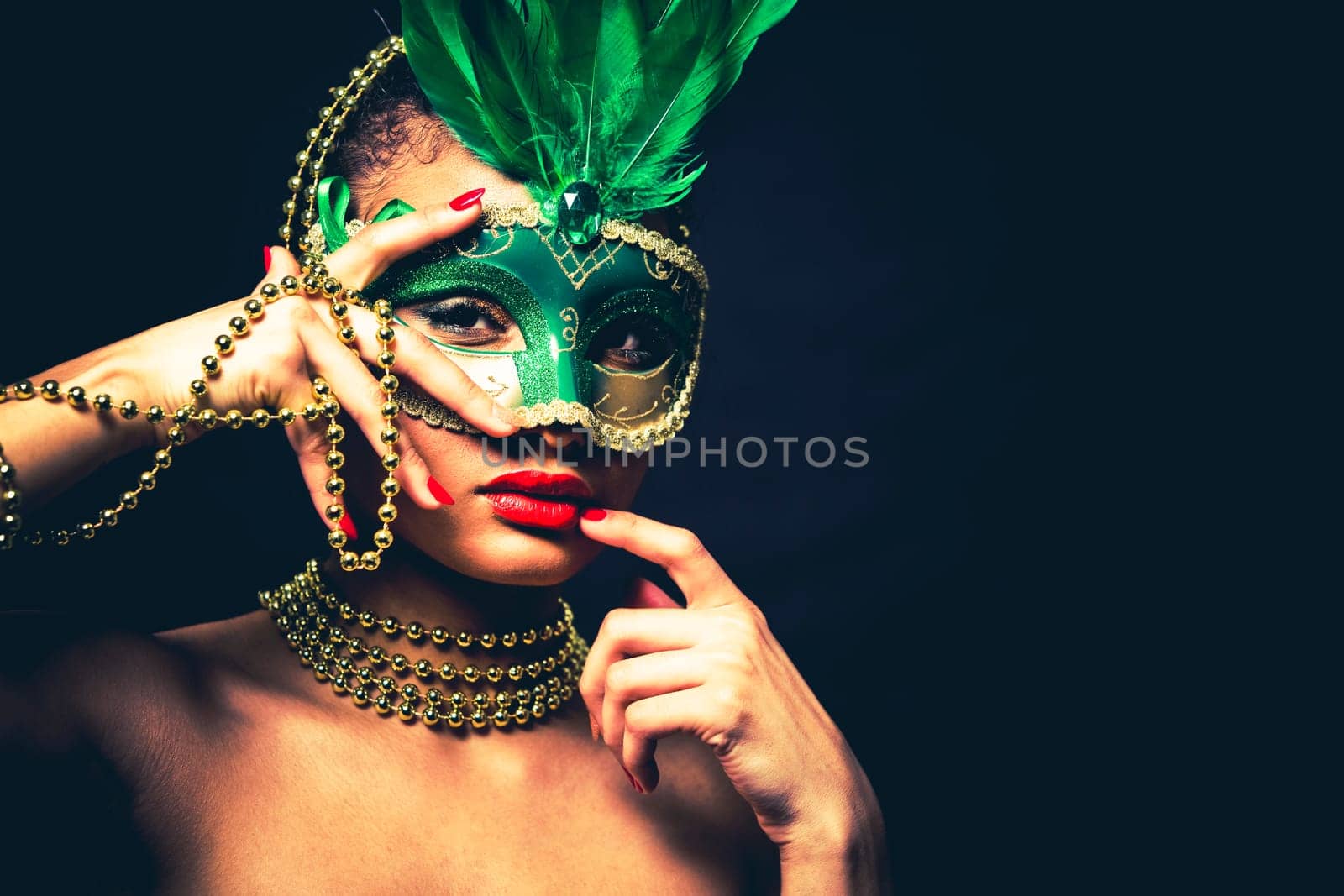 Upscale Indian woman wearing gold jewellery and red lipstick on black background. Green party mask.