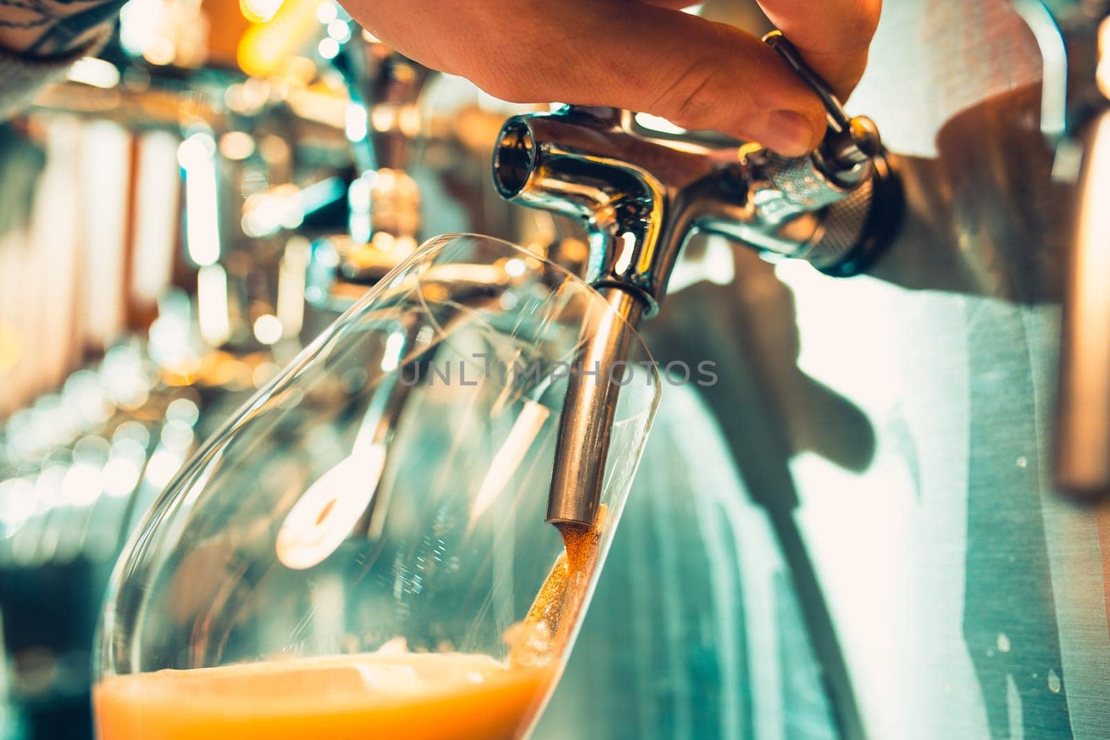 Hand of bartender pouring a large lager beer in tap. Soft, vintage instagram effect on photo. Pouring beer for client. Side view of young bartender pouring beer while standing at the bar counter