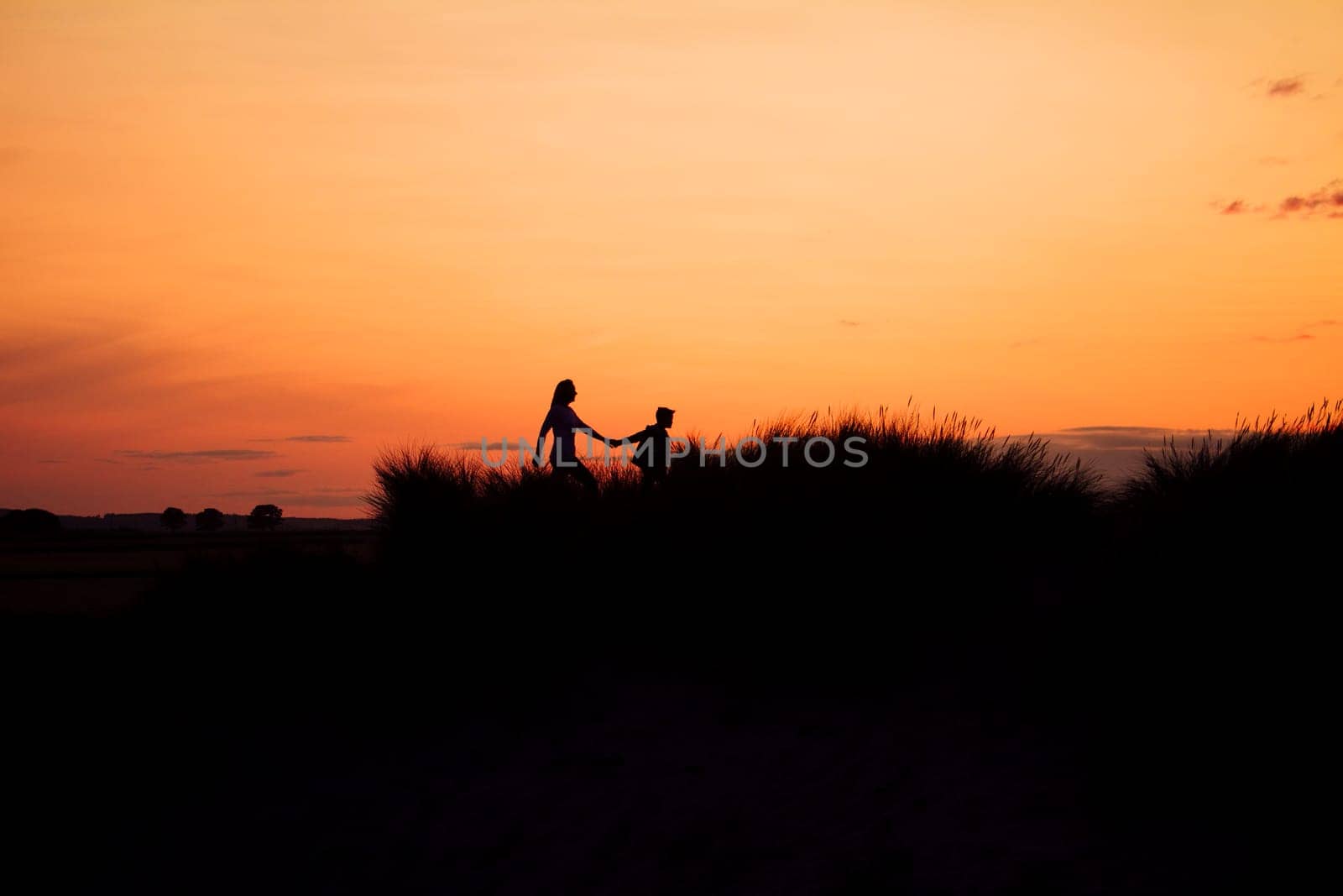 Silhouette of a mother and son walking through the sand dunes at sunset.