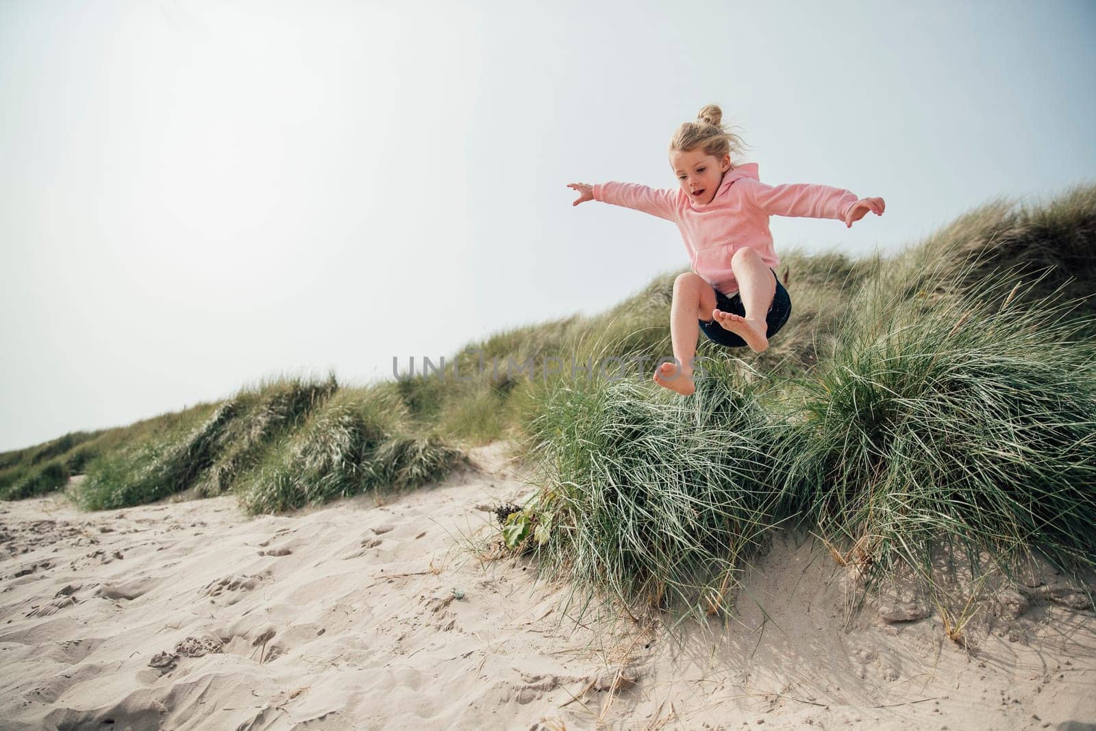 Little girl jumping over a sand dune while on holiday with her family, having some fun.