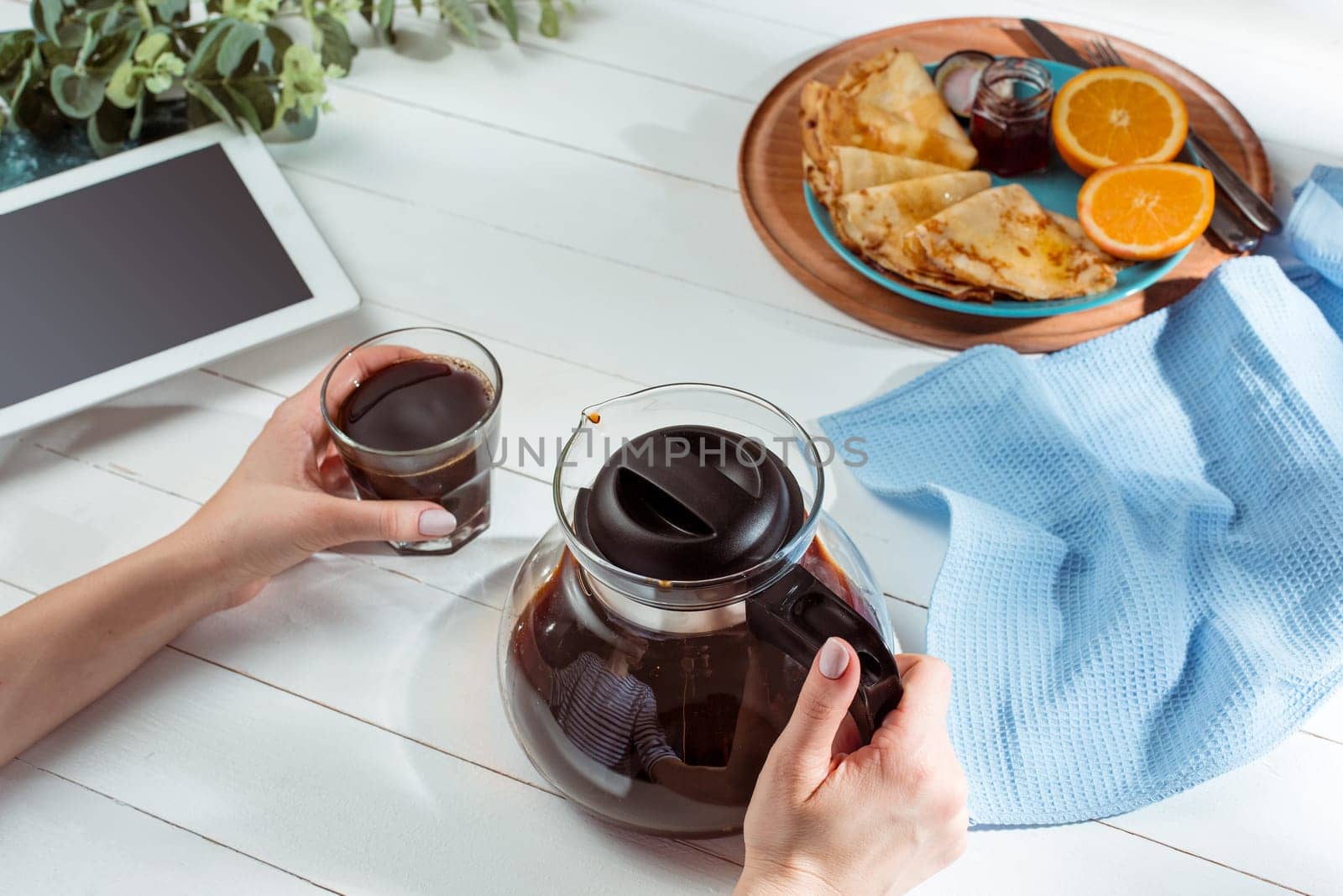 The female hands, phone and pancakes with juice nd female hands. Healthy breakfast. Fresh homemade french crepes made with ffresh fruits on a vintage wooden board on the wooden table. Top view with honey, fruits and coffee. French pancakes concept