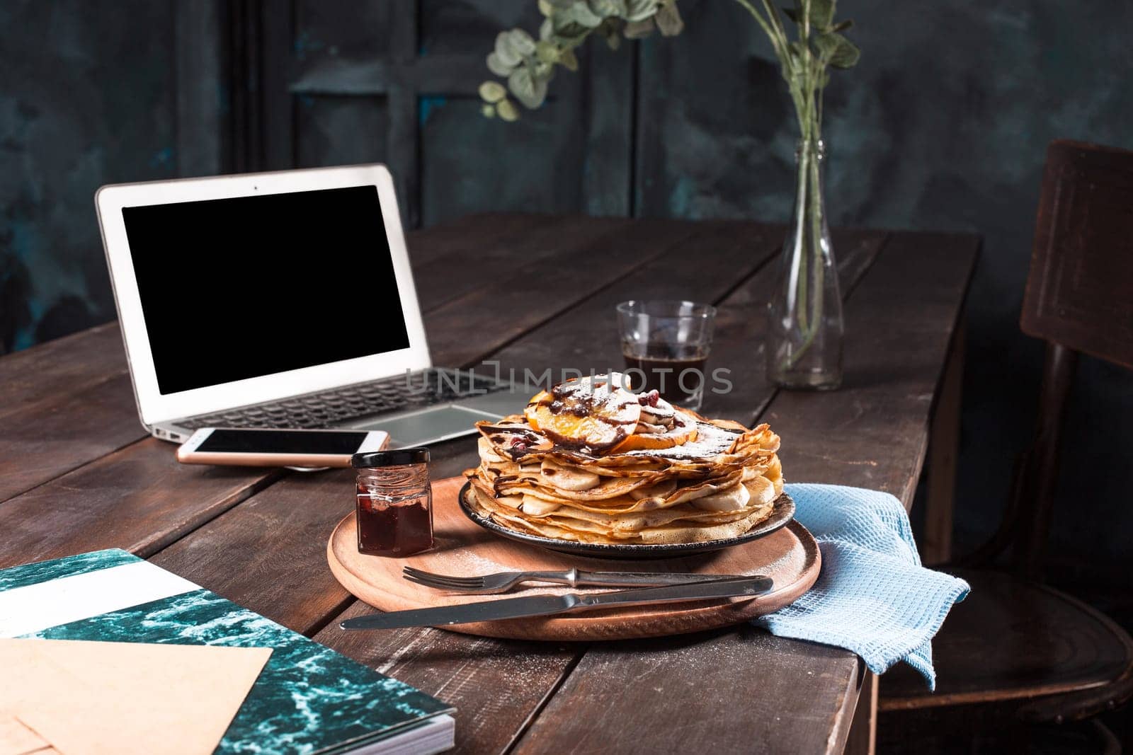 Laptop and pancakes with juice. Healthy breakfast. Fresh homemade french crepes made with ffresh fruits on a vintage wooden board on the wooden table. Side view with honey, fruits and coffee. French pancakes concept