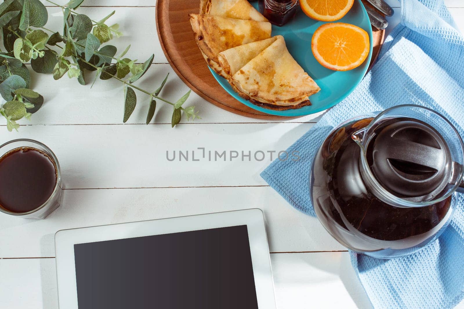 The tablet and pancakes with juice. Healthy breakfast. Fresh homemade french crepes made with ffresh fruits on a vintage wooden board on the wooden table. Top view with with honey, fruits and coffee. French pancakes concept