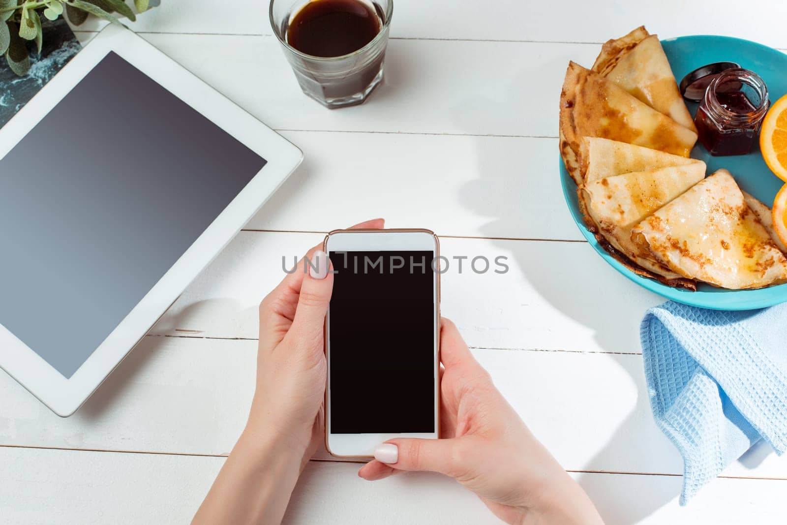 The female hands, phone and pancakes with juice nd female hands. Healthy breakfast. Fresh homemade french crepes made with ffresh fruits on a vintage wooden board on the wooden table. Top view with honey, fruits and coffee. French pancakes concept
