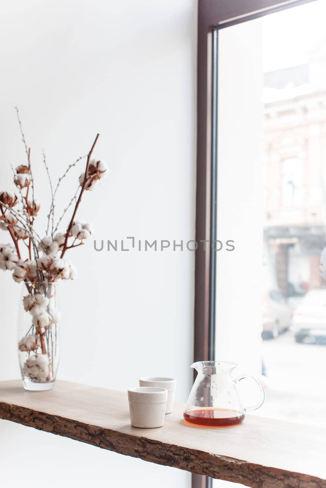 Cup of coffee, branch of tree, wooden windowsill. In the background white window.