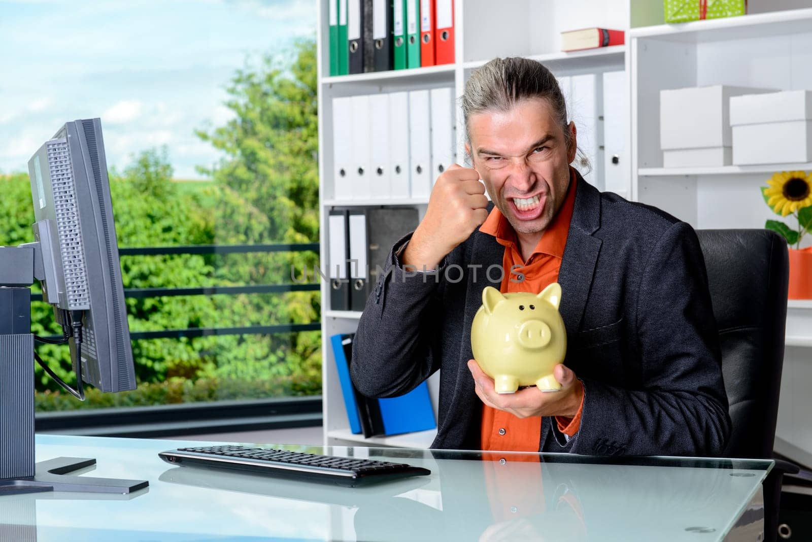 young angry business man at his desk with piggy bank