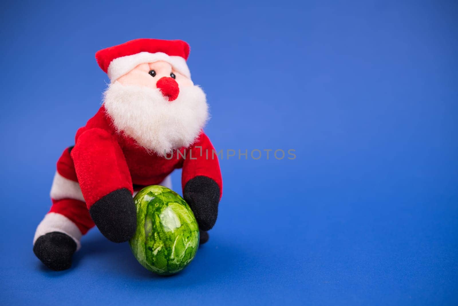little santa claus with green easter egg on blue ground