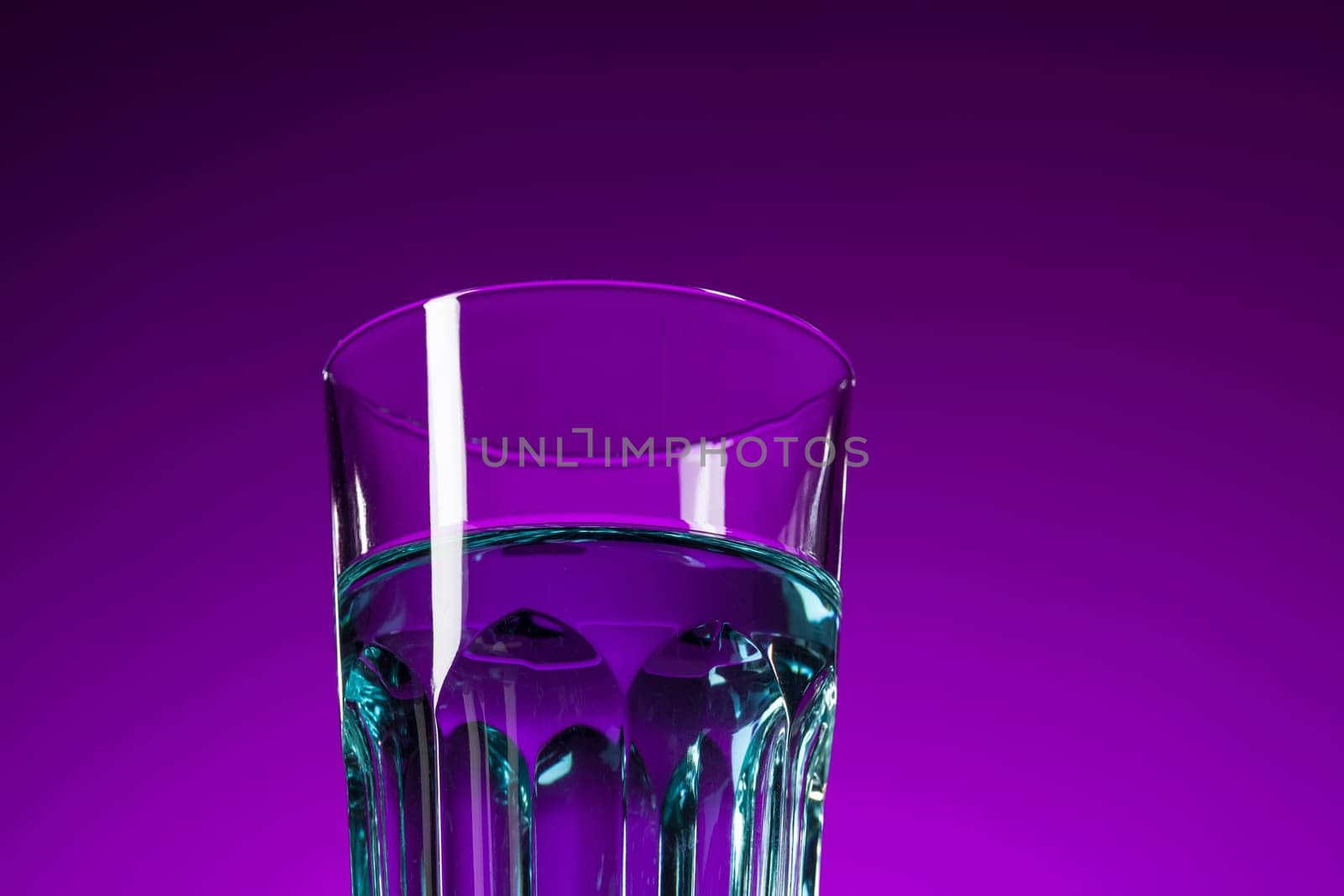 The water in glass on lilac background at studio. Vivid bright colored lighting. Trendy in 2018 Ultra Violet Light Bulb. Art decoration with tone of mystic color