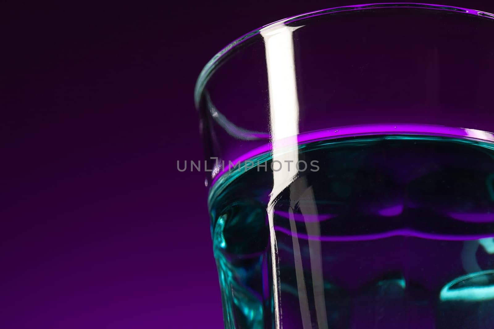 The water in glass on lilac background at studio. Vivid bright colored lighting. Trendy in 2018 Ultra Violet Light Bulb. Art decoration with tone of mystic color