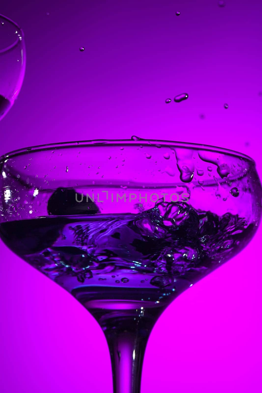 The wine stuffed glasse with cocktail standing on the table at studio. Vivid bright colored lighting. Trendy in 2018 Ultra Violet Light Bulb. Art decoration with tone of mystic color