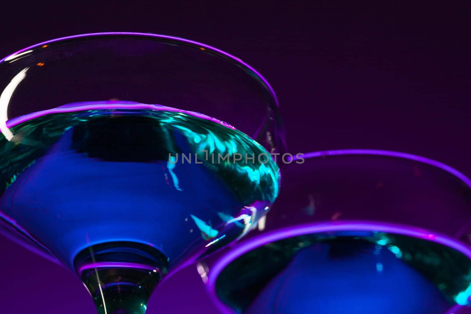 Two wine stuffed glasses standing on the table at studio. Vivid bright colored lighting. Trendy in 2018 Ultra Violet Light Bulb. Art decoration with tone of mystic color