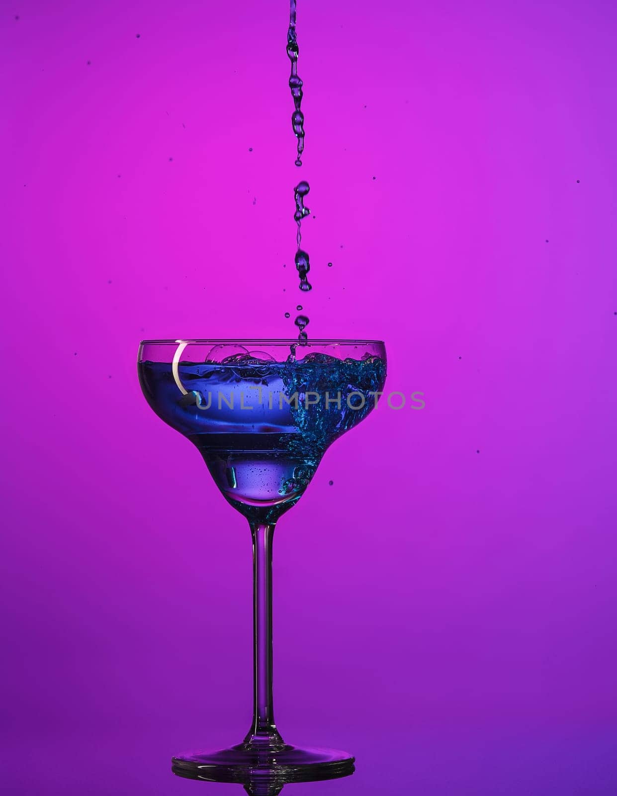 The wine stuffed glasse with cocktail standing on the table at studio. Vivid bright colored lighting. Trendy in 2018 Ultra Violet Light Bulb. Art decoration with tone of mystic color