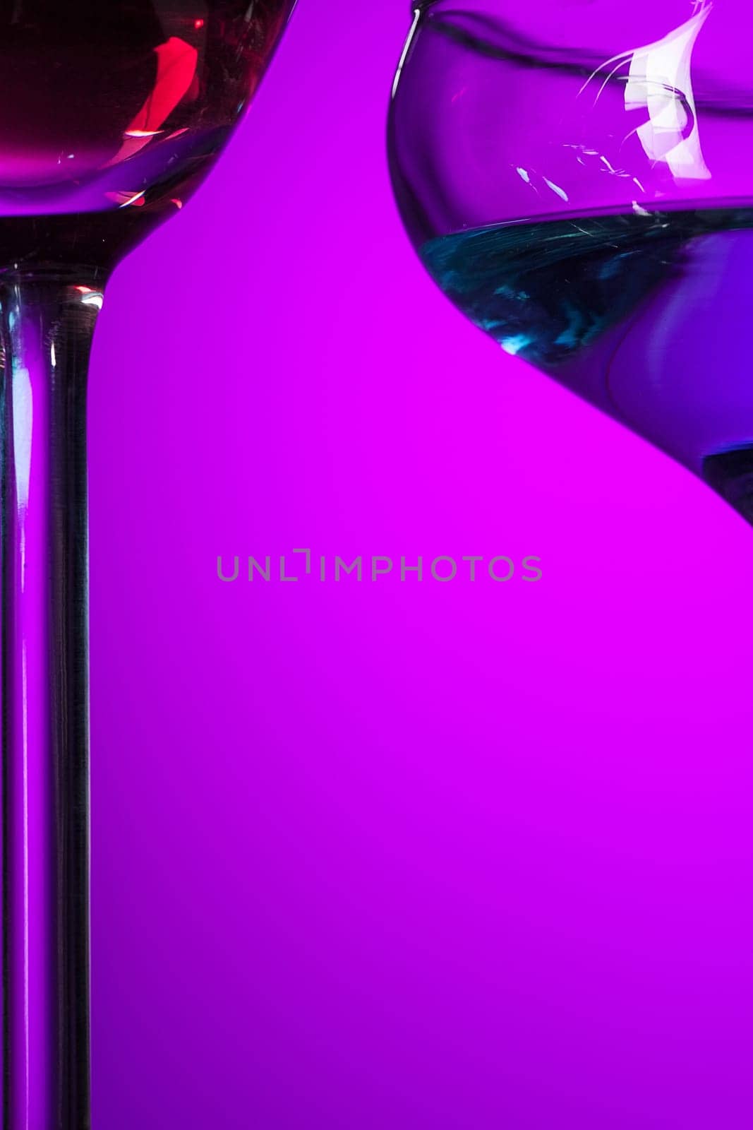Two wine stuffed glasses standing on the table at studio. Vivid bright colored lighting. Trendy in 2018 Ultra Violet Light Bulb. Art decoration with tone of mystic color