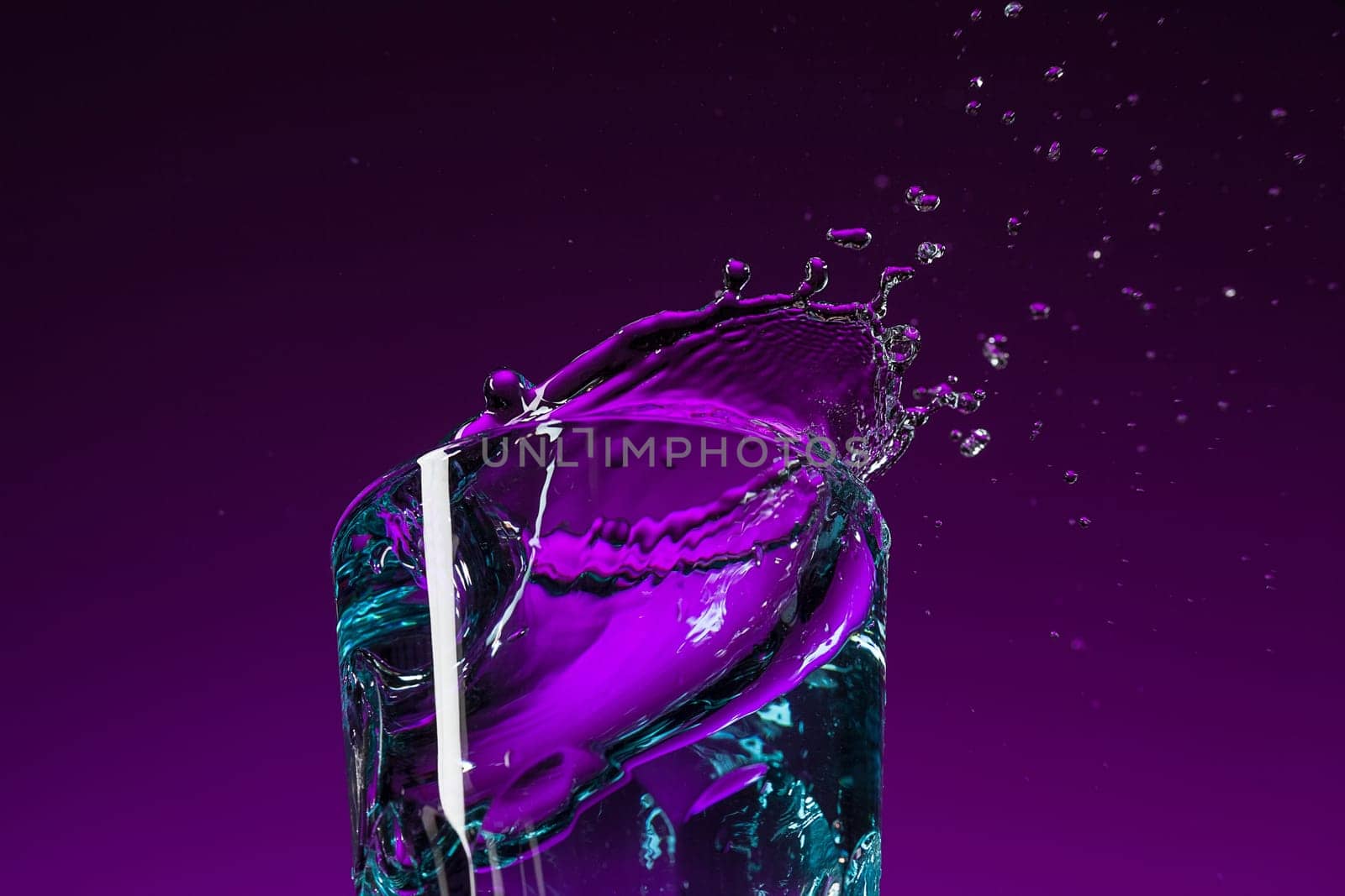 The water splashing in glass on lilac background at studio. Vivid bright colored lighting. Trendy in 2018 Ultra Violet Light Bulb. Art decoration with tone of mystic color