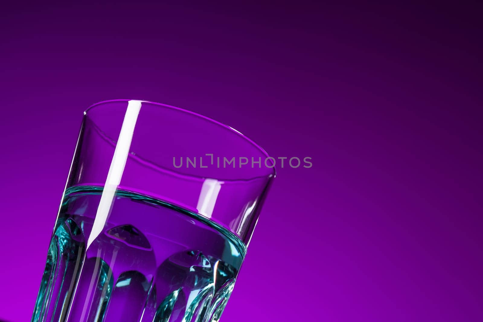 The water in glass on lilac background at studio. Vivid bright colored lighting. Trendy in 2018 Ultra Violet Light Bulb. Art decoration with tone of mystic color