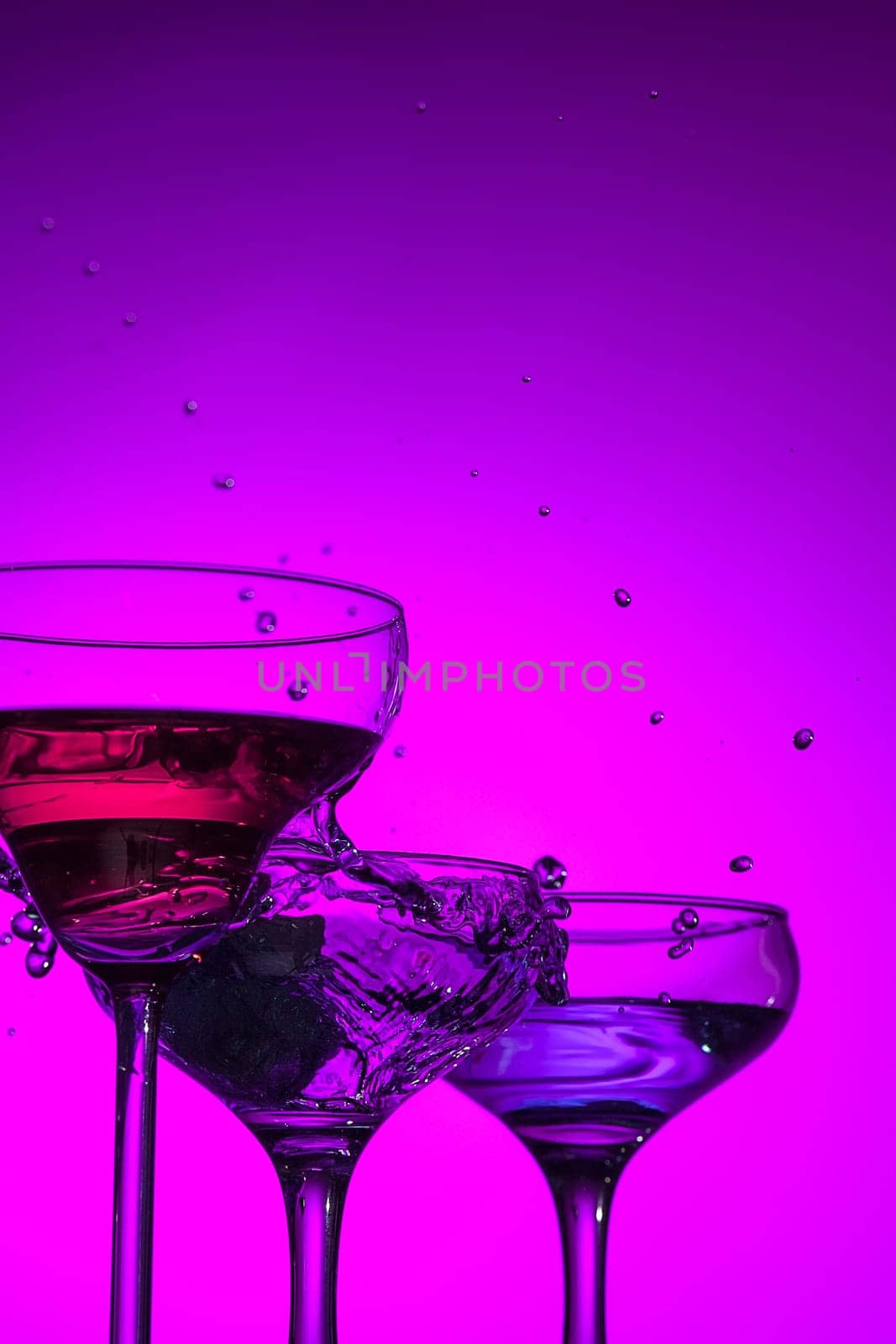 Three wine stuffed glasses standing on the table at studio. Vivid bright colored lighting. Trendy in 2018 Ultra Violet Light Bulb. Art decoration with tone of mystic color