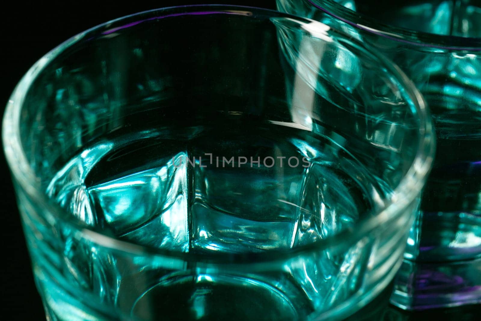 The water in two glasses on lilac background at studio. Vivid bright colored lighting. Trendy in 2018 Ultra Violet Light Bulb. Art decoration with tone of mystic color