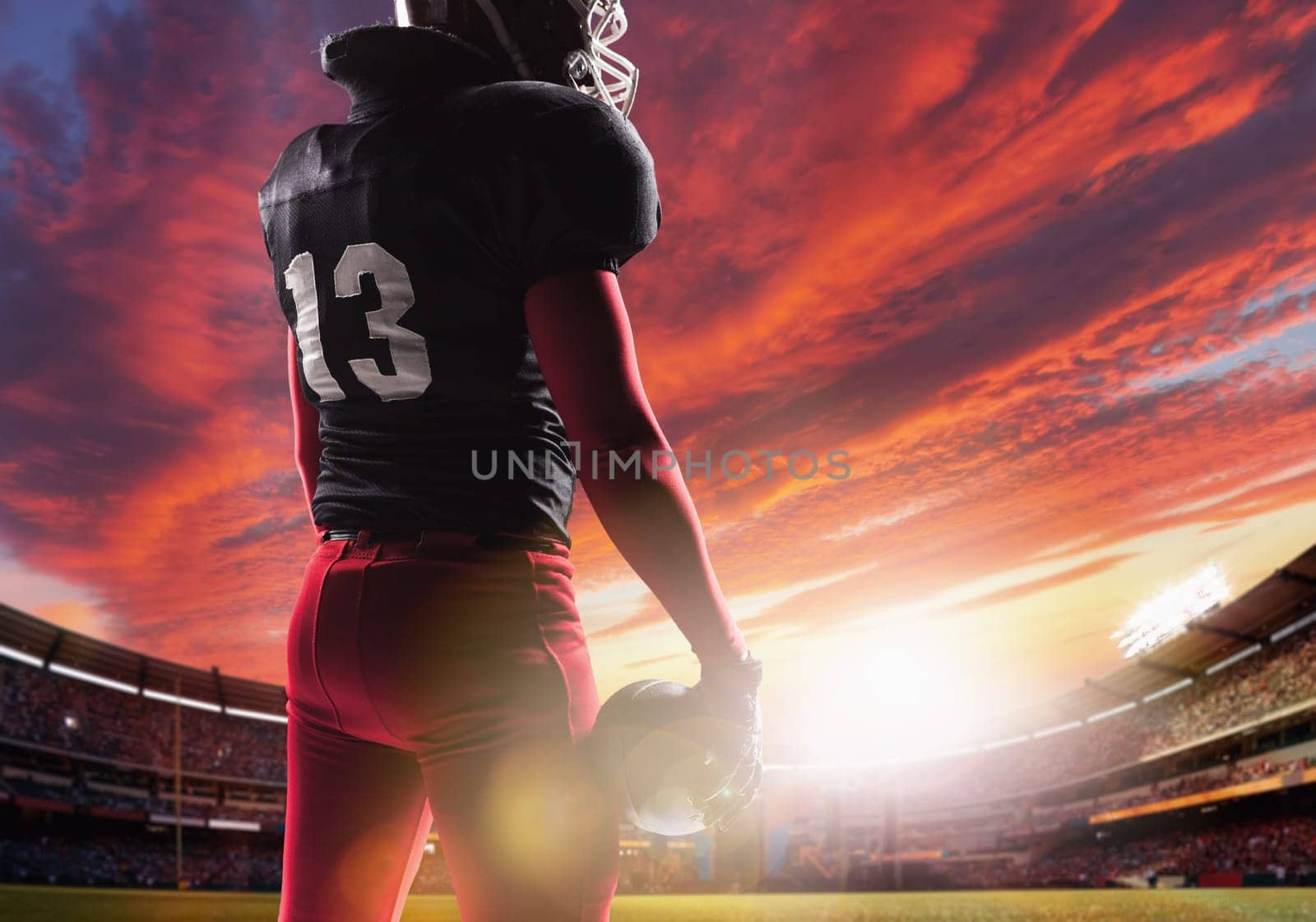 Caucasian fitness man as american football player holding a ball on stadium background at sunset