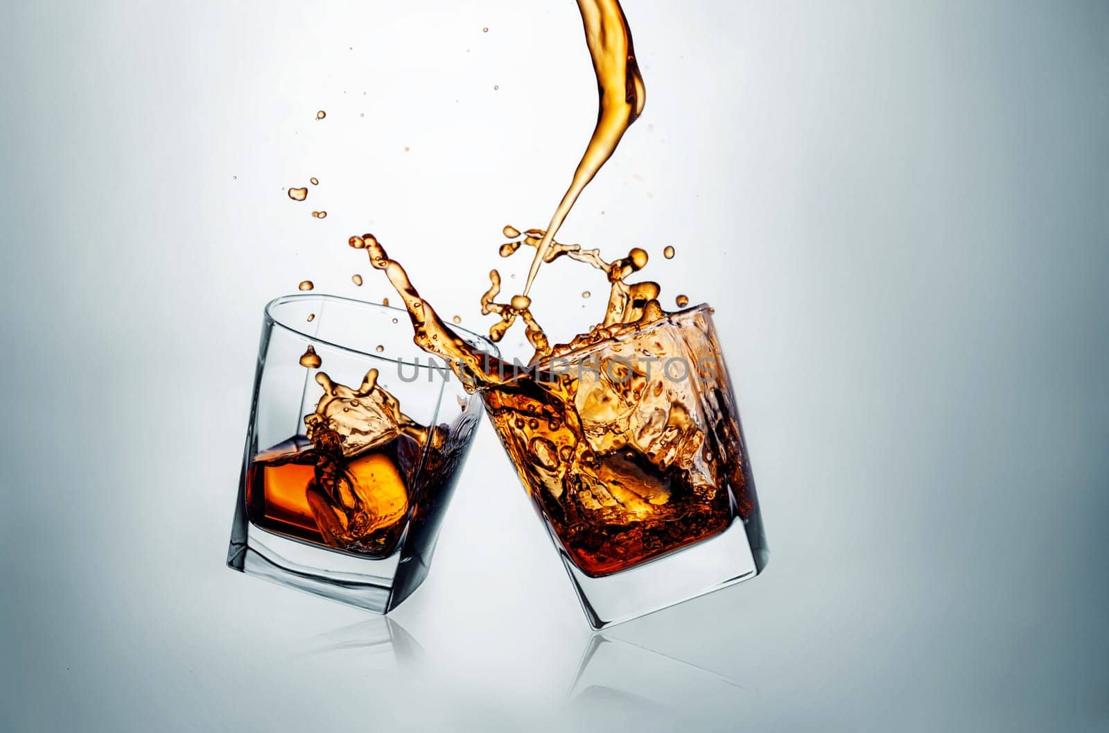 Two whiskey glasses clinking together on gray studio background