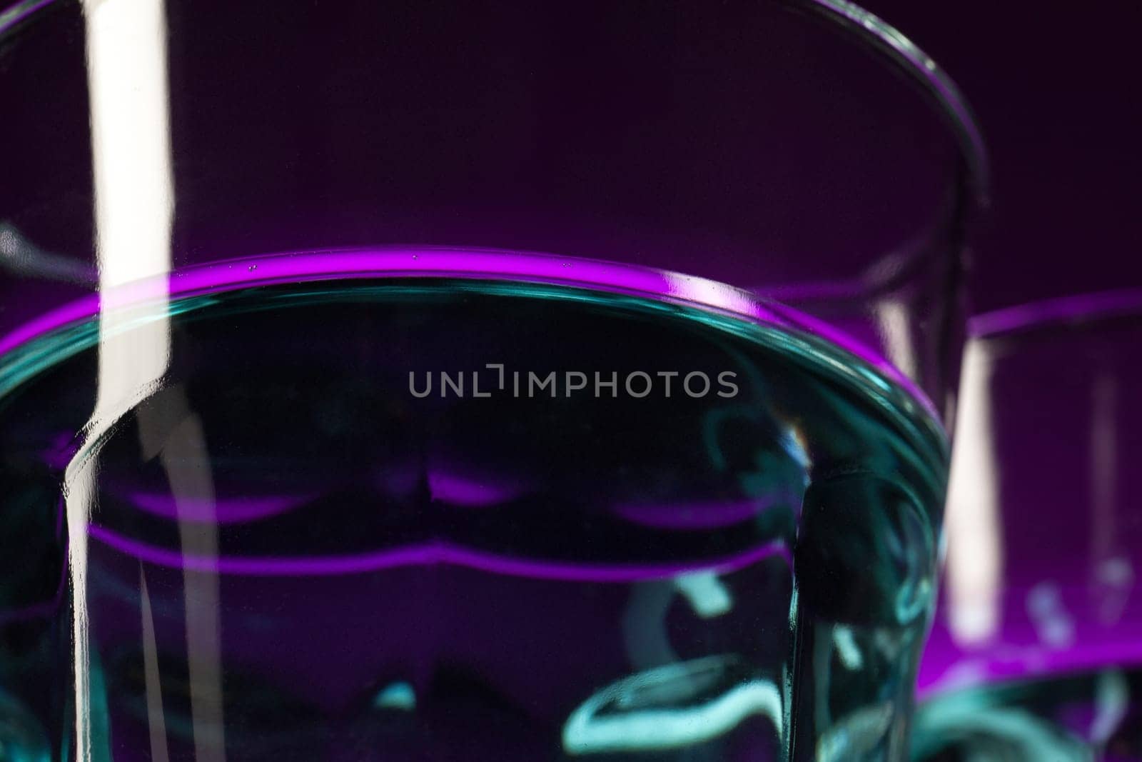 Two wine stuffed glasses standing on the table at studio. Vivid bright colored lighting. Trendy in 2018 Ultra Violet Light Bulb. Art decoration with tone of mystic color