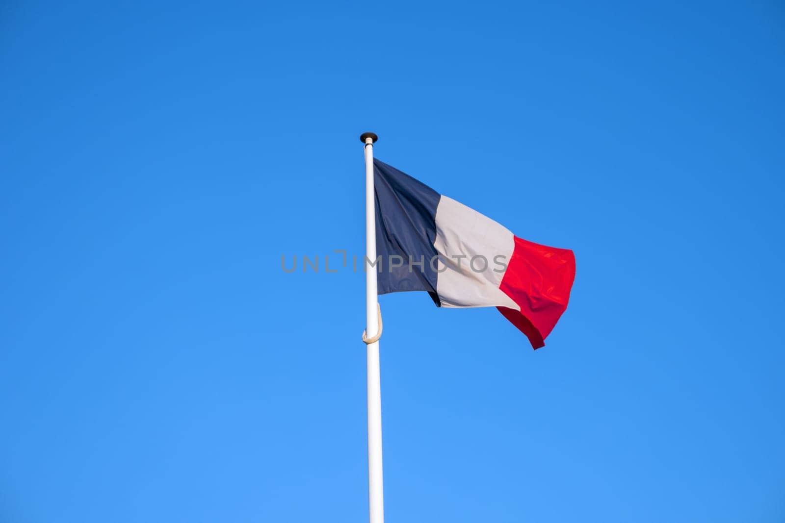 French national official flag on blue sky background. Symbol of France. Patriotic french banner, design. Flag of France on flagpole waving in the wind