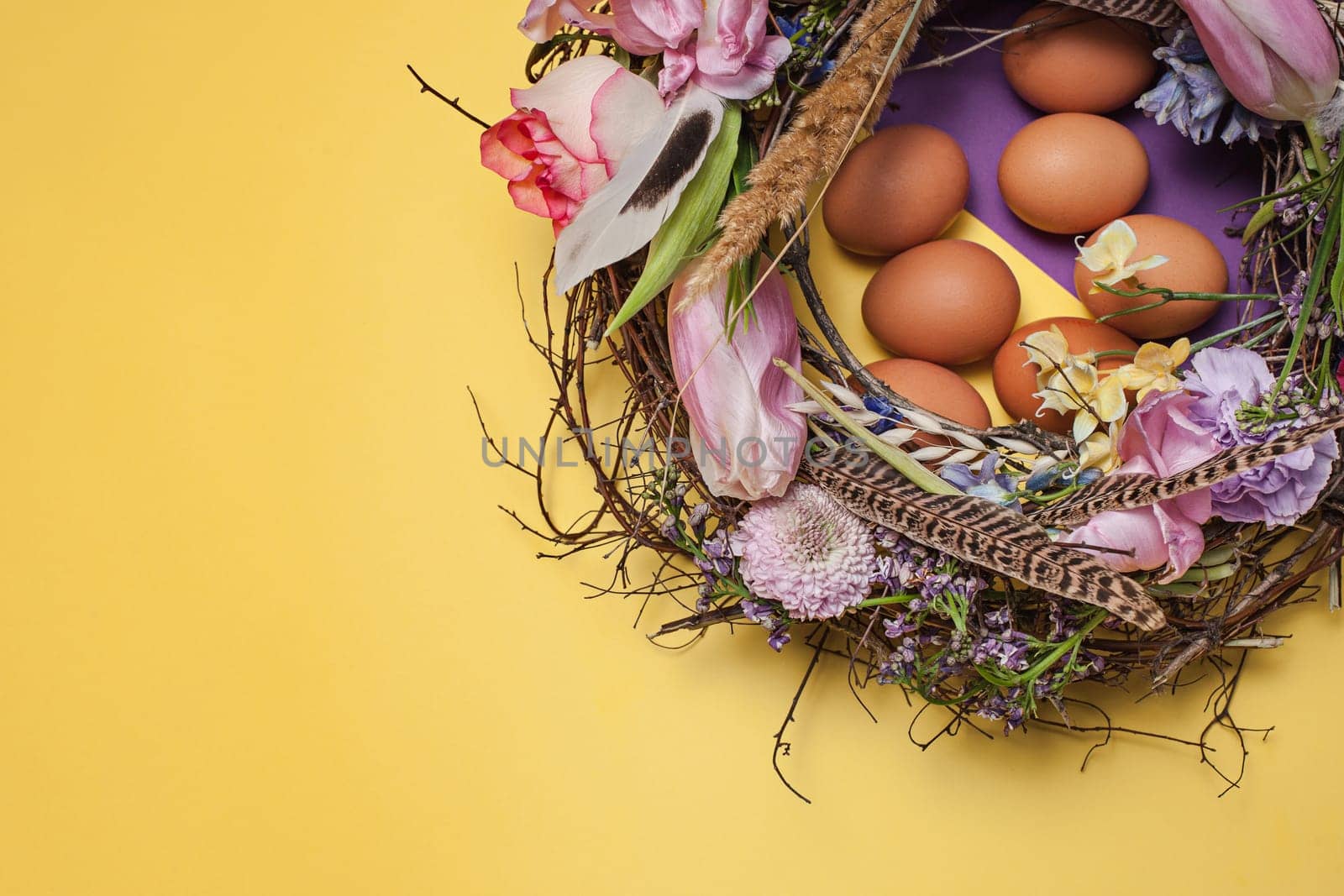 Easter card. Painted Easter eggs in nest on yellow table background. Top view of easter decoration. Happy easter concept