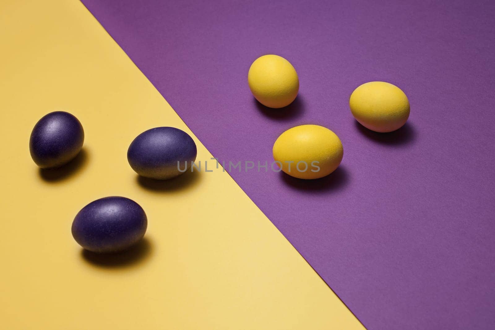 Beautiful easter table setting composition. A row of lilac and yellow color eggs on lviolet and yellow background. Happy Easter greeting card. Top view, copy space.