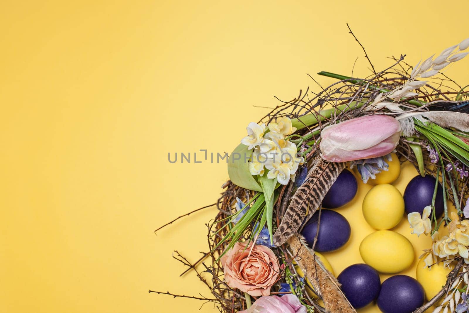 Easter card. Painted Easter eggs in nest on yellow table background. Top view of easter decoration. Happy easter concept
