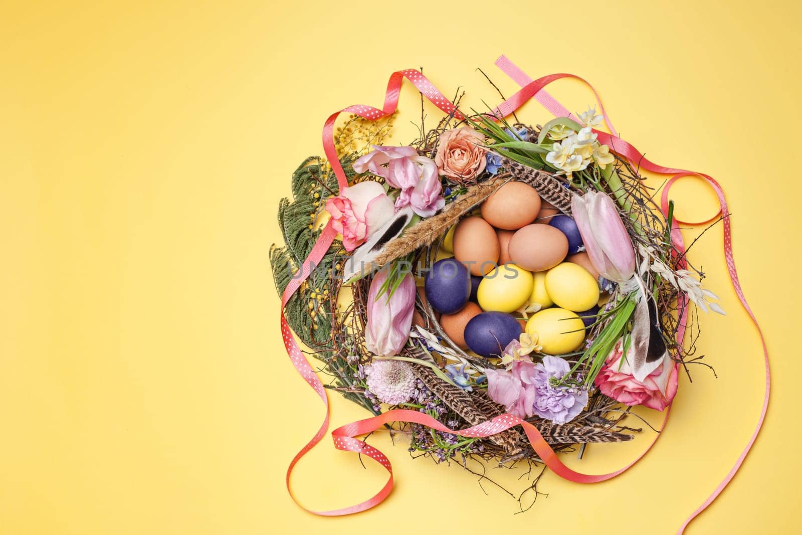 Easter card. Painted Easter eggs in nest on yellow table background. Top view of easter decoration. Happy easter concept