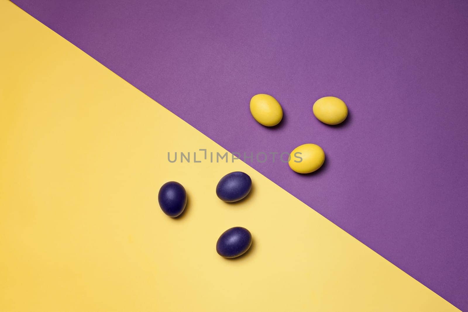 Beautiful easter table setting composition. A row of lilac and yellow color eggs on lviolet and yellow background. Happy Easter greeting card. Top view, copy space.