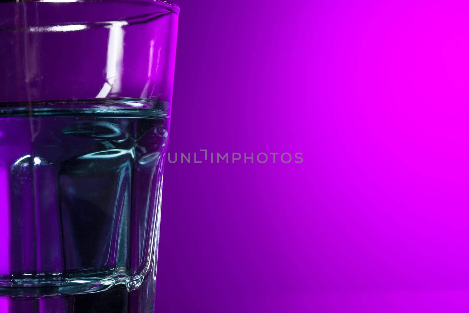 The water in glass on lilac background at studio. Vivid bright colored lighting. Trendy in 2018 Ultra Violet Light Bulb. Art decoration with tone of mystic color