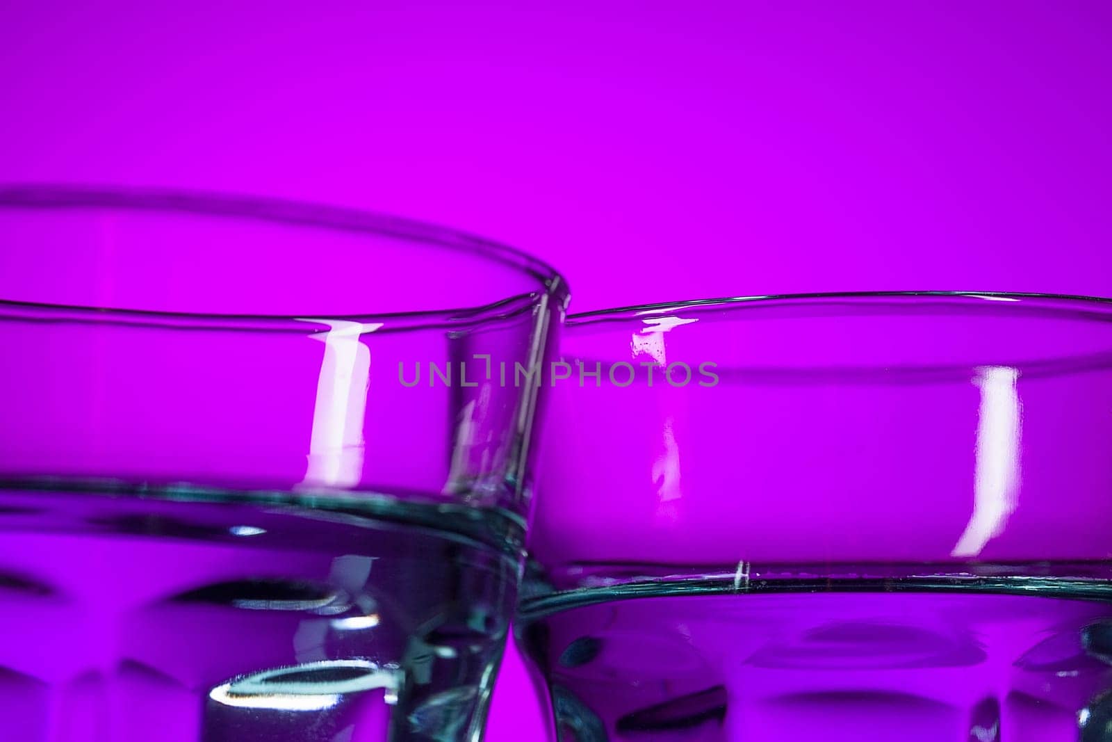 The water in two glasses on lilac background at studio. Vivid bright colored lighting. Trendy in 2018 Ultra Violet Light Bulb. Art decoration with tone of mystic color