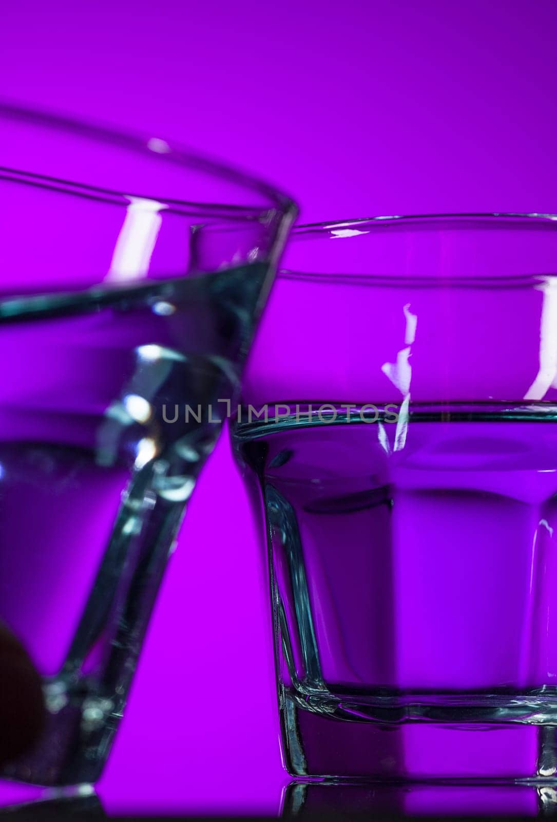 The water in two glasses on lilac background at studio. Vivid bright colored lighting. Trendy in 2018 Ultra Violet Light Bulb. Art decoration with tone of mystic color