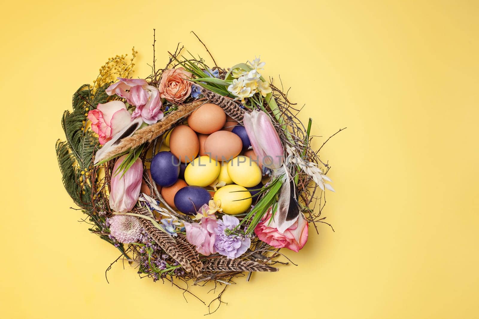 Easter card. Painted Easter eggs in nest on yellow table background. Top view of easter decoration. Happy easter concept