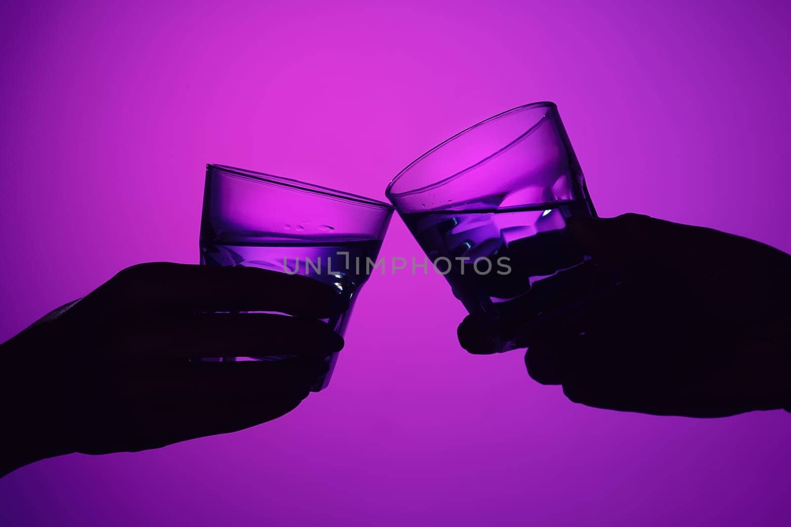 Two wine stuffed glasses and female and male hands at studio. Vivid bright colored lighting. Trendy in 2018 Ultra Violet Light Bulb. Art decoration. concept of toast