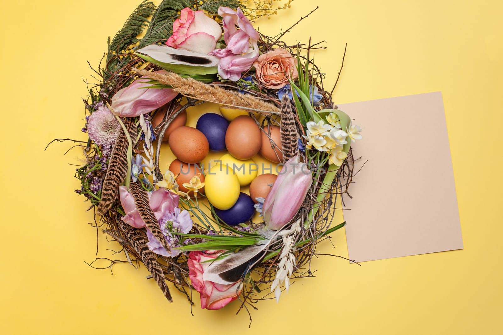 Easter card. Painted Easter eggs in nest on yellow table background. Top view of easter decoration. Happy easter concept