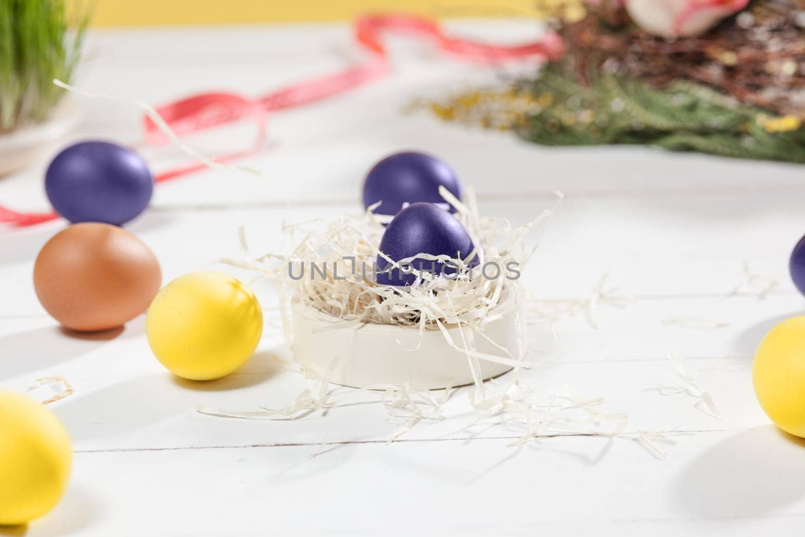 Beautiful easter table setting composition. A row of lilac and yellow color eggs on white wooden table background. Happy Easter greeting card. Side view